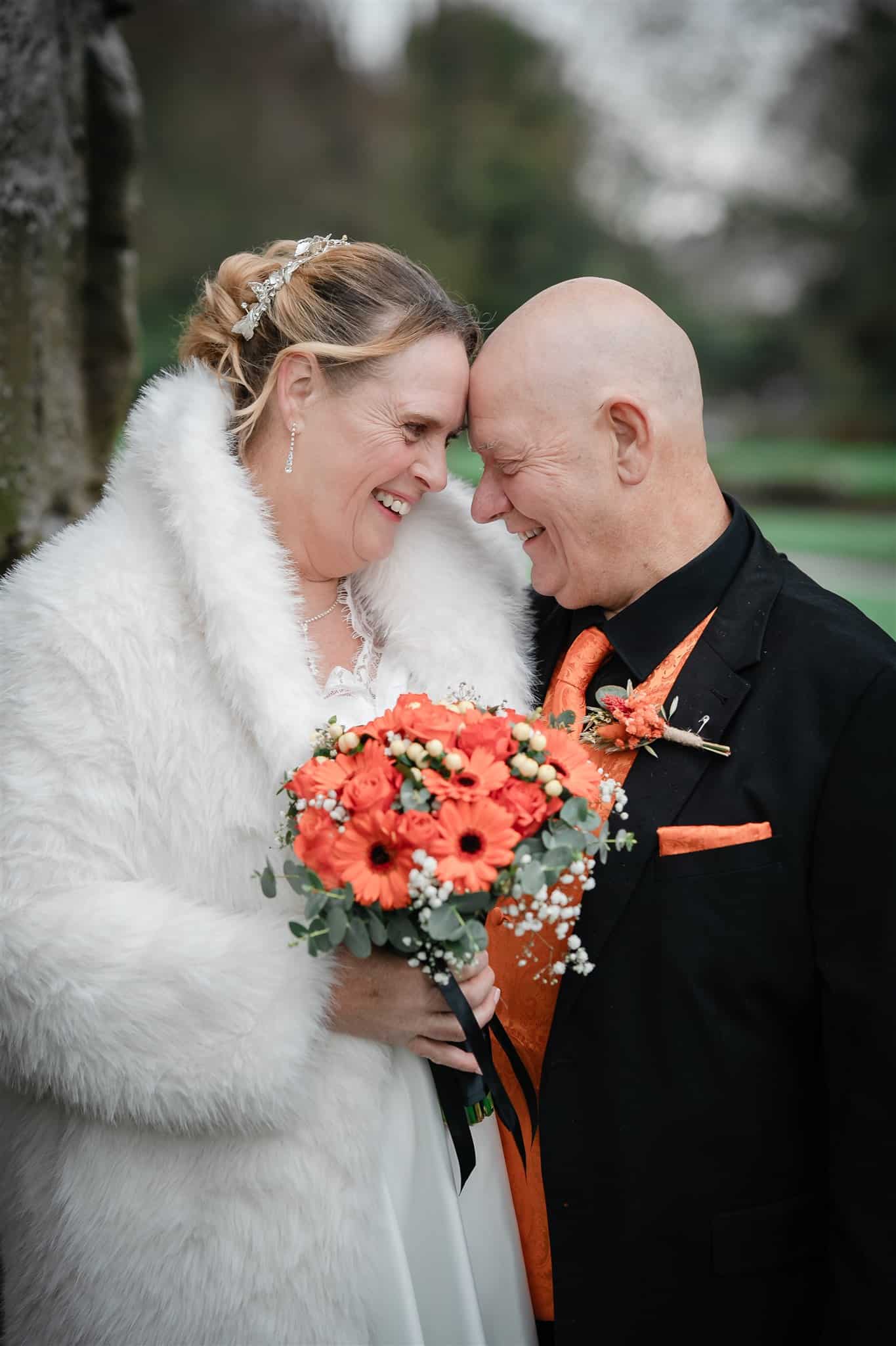 Wedding couple smiling and holding a bouquet in a scenic outdoor setting.