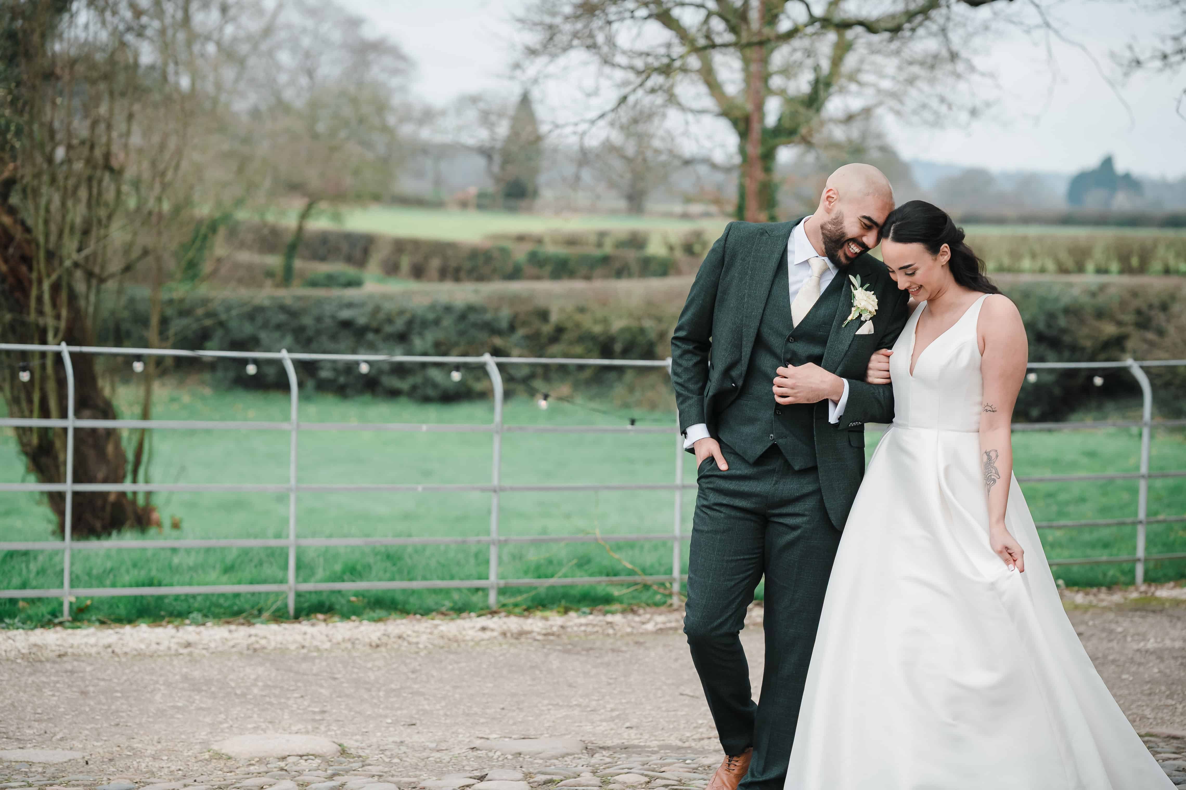 Wedding couple walking outdoors in a rural setting, smiling and holding hands.