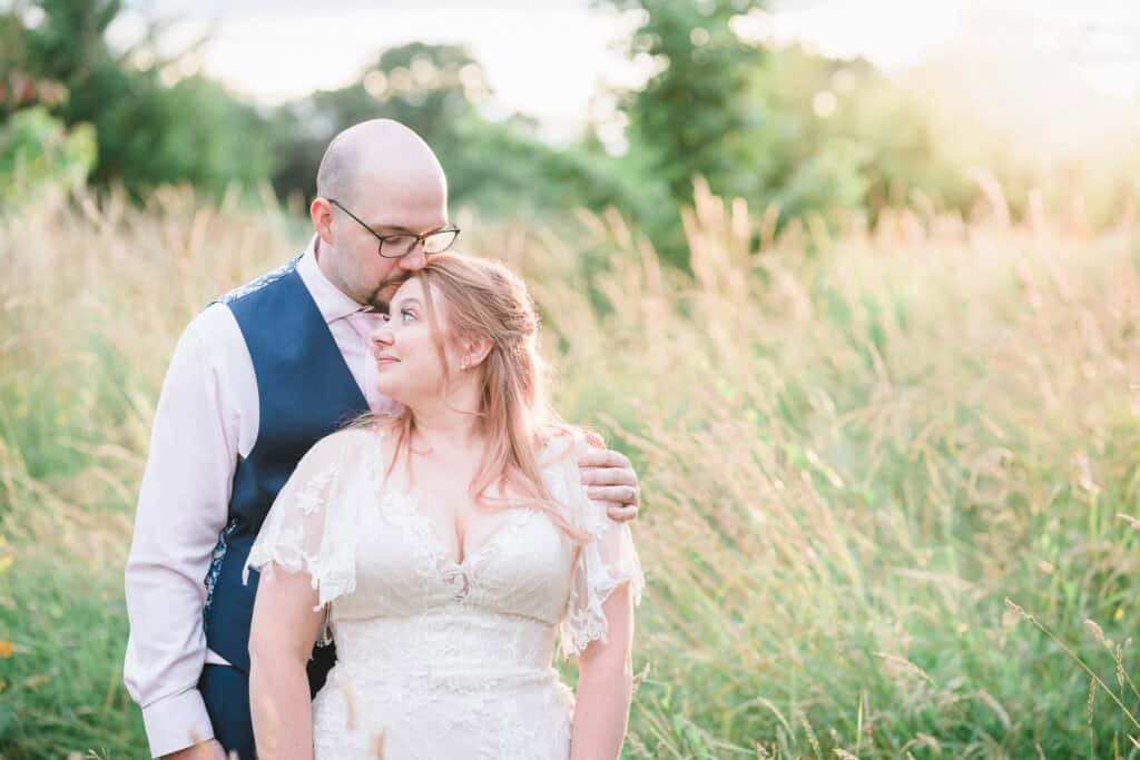 a bride and groom kiss in a field on their wedding day