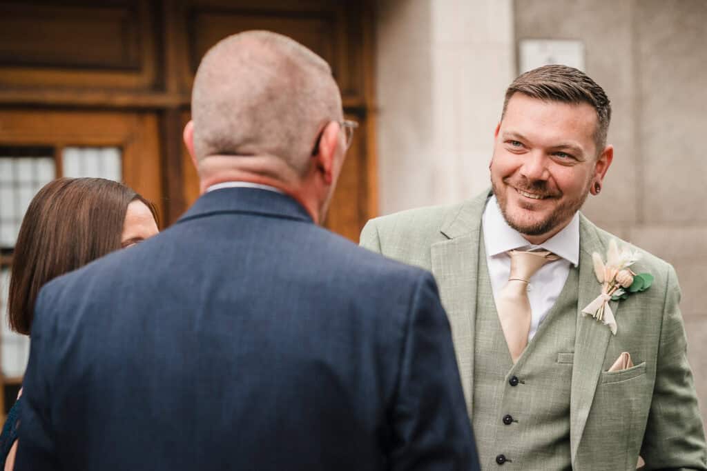 a groom smiles at a friend outside islington town hall