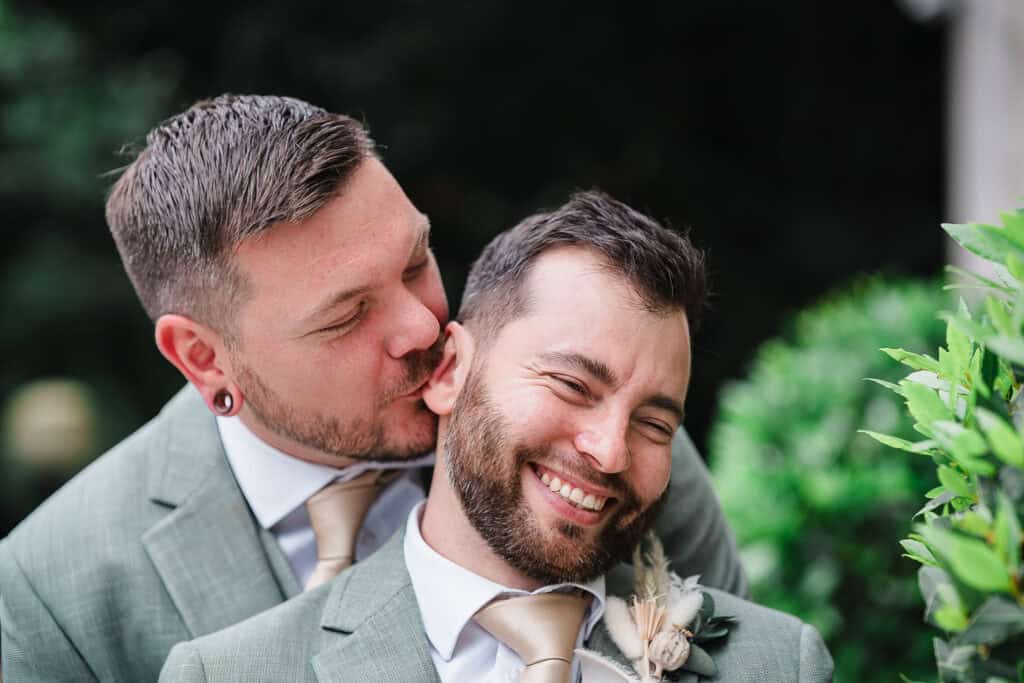 a groom kisses his husbands ear at a wedding in islington town hall
